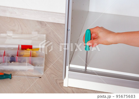 Repairs in house or apartment. Female hand repairing white furniture with a screwdriver in home, close up. Diy concept. Repairs in house or apartment. Female hand repairing white furniture with a screwdriver in home, close up. Diy concept. 95675683