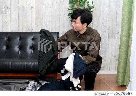 スーツケースの前で服選びを迷う男性 95676067