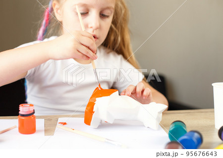 a little girl paints a toy fox made of clay. DIY concept 95676643