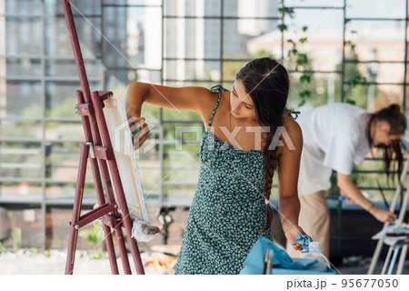 Young woman artist paints with a spatula on the canvas Young woman artist paints with a spatula on the canvas 95677050