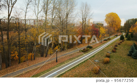 Autumn city park. Trees with colorful leaves. A cycle path winds between the trees. Autumn landscape. Aerial photography. 95677250