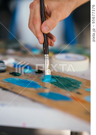 Artist mixes paints with a brush on a palette Artist mixes paints with a brush on a palette 95677376