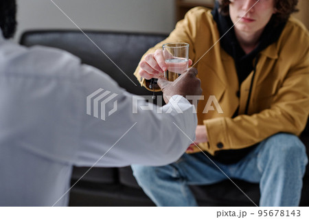 Close-up of teenage boy drinking water while talking to psychologist at office 95678143
