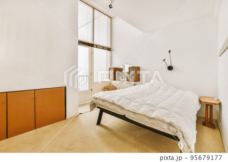 Home interior design of bedroom with bed and wooden wardrobe placed in corner near window in modern apartment 95679177