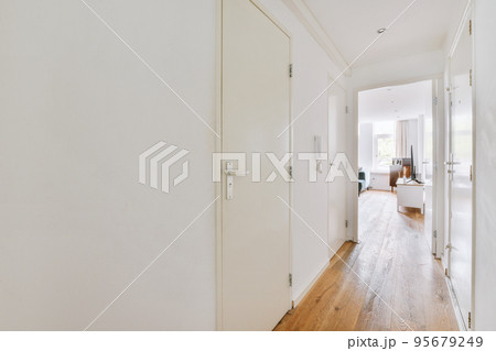 Light narrow hallway with many doors in white walls and glowing lamp over lumber floor 95679249