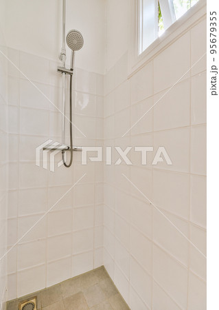 Shower faucets attached to tiled wall near glass partition and ornamental curtail in washroom at home 95679355