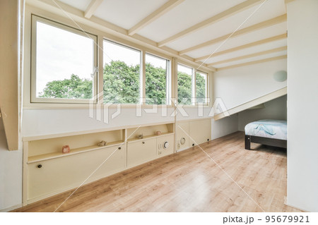 Bed placed near wall in modern minimalist style mansard bedroom with windows 95679921