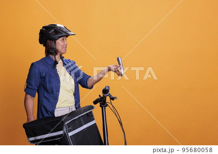 Restaurant employee with blue uniform and helmet delivering fast food order giving POS terminal to customer. Pizzeria employee using bike as transportation while carrying takeout food backpack Restaurant employee with blue uniform and helmet delivering fast food order giving POS terminal to customer. Pizzeria employee using bike as transportation while carrying takeout food backpack 95680058