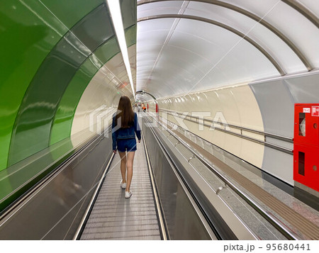 A beautiful girl walks along the travolator in the subway tunnel to go to another underground station. View from the back 95680441