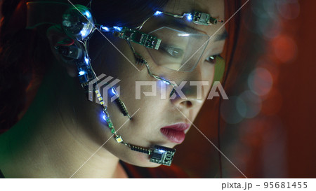 Focused asian girl in cyberpunk attire and futuristic glasses works on computer Focused asian girl in cyberpunk attire and futuristic glasses works on computer 95681455