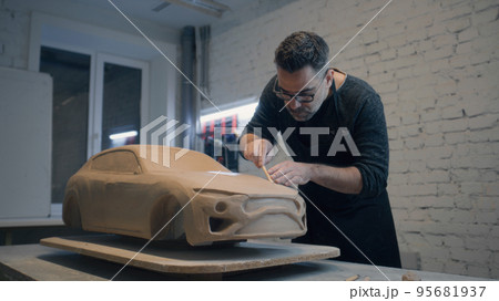 Experienced designer works on the sculpture of the car using wooden shaping tool Experienced designer works on the sculpture of the car using wooden shaping tool 95681937
