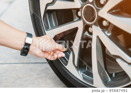 driver hand inflating tires of vehicle, removing tire valve nitrogen cap for checking air pressure and filling air on car wheel at gas station. self service, maintenance and safety 95687491