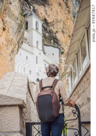 Man tourist in Monastery of Ostrog, Serbian Orthodox Church situated against a vertical background, high up in the large rock of Ostroska Greda, Montenegro. Dedicated to Saint Basil of Ostrog 95687817