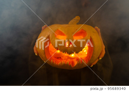 The witch is holding a pumpkin jack about a lantern glowing in the dark. Halloween. The witch is holding a pumpkin jack about a lantern glowing in the dark. Halloween. 95689340