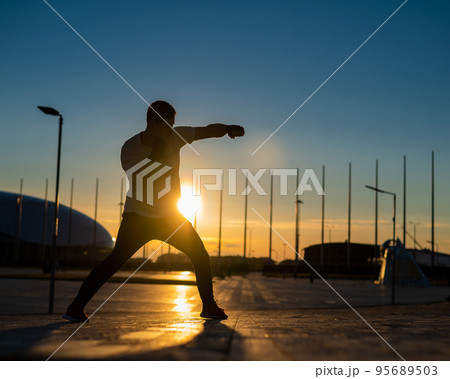 A man trains boxing at sunset outdoors. 95689503