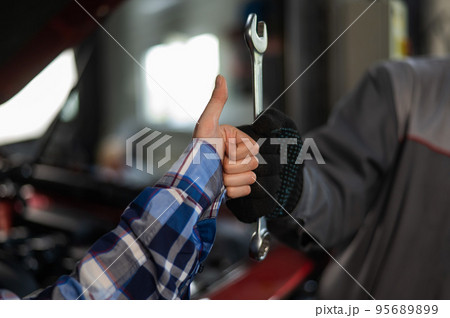 Close-up of woman's hand thumb up and mechanic's hand with tool. Automotive master in gloves shows a positive gesture after finishing work 95689899