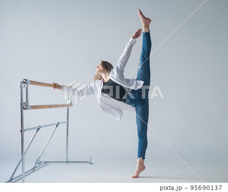 Caucasian woman in casual clothes pulls the split at the ballet barre.  95690137