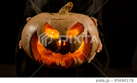 The witch is holding a pumpkin jack about a lantern glowing in the dark. Halloween. 95690178