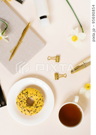 Women's desktop of a fashion blogger or a freelance girl. Stationery, notepad, cup of tea and donut. 95690854