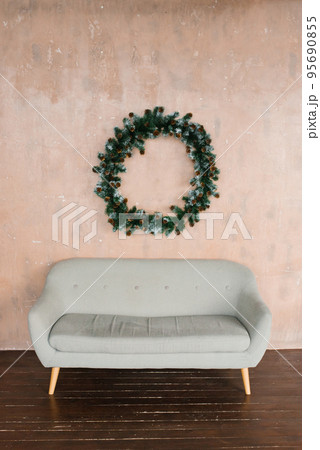 Laconic interior of the living room. Grey sofa and a Christmas wreath on the wall 95690855