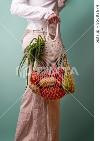 Woman hold mesh bag with vegetables and herbs. Woman hold mesh bag with vegetables and herbs. 95692674