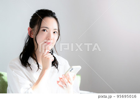 スマホをもって考えるかわいい女性　 95695016