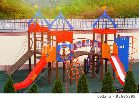 Colorful playground on yard in city. Children playground surrounded by green trees in sunlight in summer. Colorful playground on yard in city. Children playground surrounded by green trees in sunlight in summer. 95695599