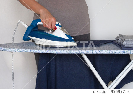 Clothing ironing at home. Young girl is ironing garments at home. Female hand is ironing clothes, close up. 95695718