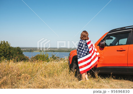 Young woman with USA flag near car enjoying nature. 95696830