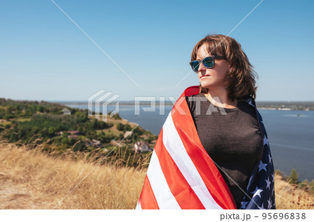 Young woman with the flag of america and in sunglasses on the nature on a sunny day. Free lifestyle Young woman with the flag of america and in sunglasses on the nature on a sunny day. Free lifestyle 95696838