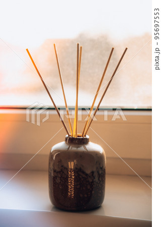 Cozy home decorations aroma reed diffuser in the living room. Home comfort concept. Bottle container with wood stick diffusers Essential oils to scent your home Minimalist air freshener concept. 95697553