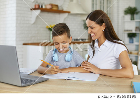 Smiling mom is helping her son doing homework studying online using laptop in home kitchen. 95698199