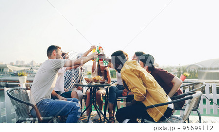 Happy girls and guys careless students are having rooftop party toasting and drinking enjoying free time in summer. Conversation, youth and celebration concept. 95699112