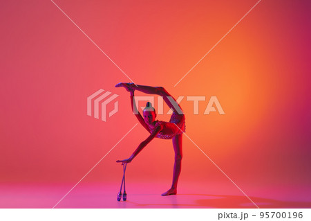 Emotions in motion. Portrait of junior female gymnast in black sport swimsuit doing gymnastics excercises isolated over pink background. Sport, skills, achievements Emotions in motion. Portrait of junior female gymnast in black sport swimsuit doing gymnastics excercises isolated over pink background. Sport, skills, achievements 95700196