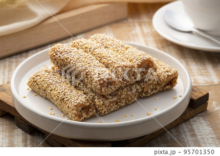 Golden brown roasted sesame seeds and peanuts are bound together by sugar to form delicious sesame bars,Thai snacks,Sesame Roll on white plate 95701350