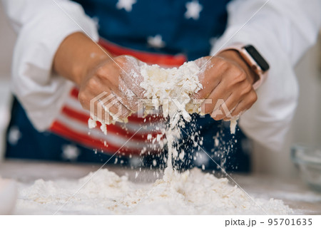 Young housewife in an apron kneads dough with her hands. Young housewife in an apron kneads dough with her hands. 95701635