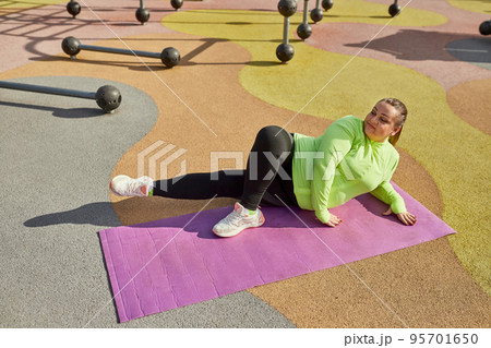 Happy overweight young woman doing fitness exercises at street public sports ground, outdoors. Sunny autumn day. Sport, health, mood, body positive 95701650
