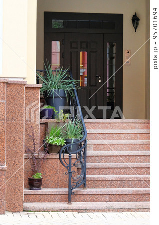 Pots of flowers and plants stand on the steps at the entrance to the house. Residential porch design. 95701694