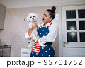 Smiling woman in kitchen holding cute white Maltese dog 95701752