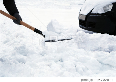 Winter problems of car drivers. Man with shovel clears snow around car in parking lot in winter after snowfall. Shovel in hand. 95702011