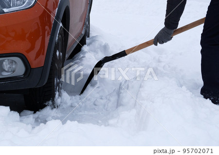 Winter, snow, vehicle. Man brushing and shoveling snow beside orange car in winter after snowfall. Shovel in hand. Winter, snow, vehicle. Man brushing and shoveling snow beside orange car in winter after snowfall. Shovel in hand. 95702071