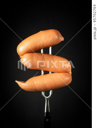 Boiled milk sausages on a fork on a black background. Fast food delicious food concept 95702764
