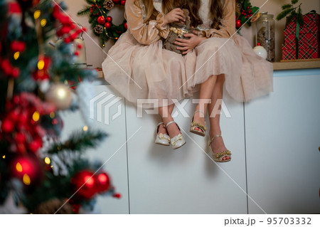 Two cute little girls in beige dresses are sitting on the table holding cookies. New Year decoration. Luxurious New Year's interior. Two cute little girls in beige dresses are sitting on the table holding cookies. New Year decoration. Luxurious New Year's interior. 95703332