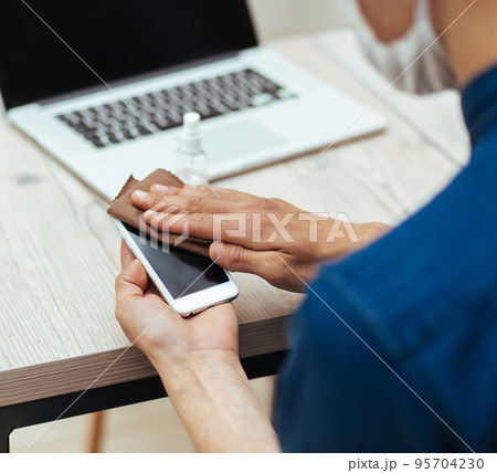 close up. a young man in a protective mask wiping the screen of his smartphone. close up. a young man in a protective mask wiping the screen of his smartphone. 95704230