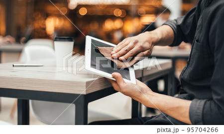 man in protective mask wiping the screen of a digital tablet with antiseptic man in protective mask wiping the screen of a digital tablet with antiseptic 95704266