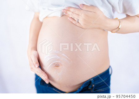 カジュアルな服装で妊娠線予防クリームを塗る妊婦 斜め1（本物の臨月妊婦さんを撮影） 95704450