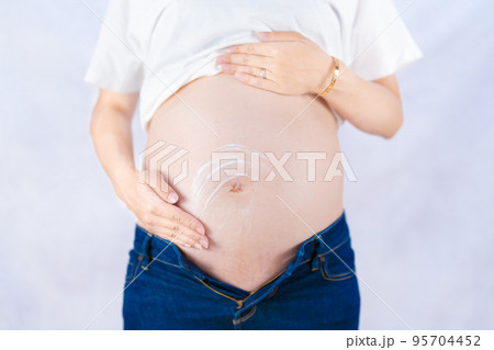 カジュアルな服装で妊娠線予防クリームを塗る妊婦 正面（本物の臨月妊婦さんを撮影） 95704452