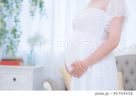 マタニティドレスでお腹に手をあてる妊婦 室内1（本物の臨月妊婦さんを撮影） 95704458
