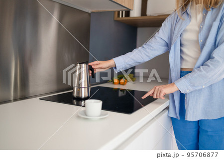 Cropped photo of a woman hands pouring coffee from a pot while standing in the kitchen. Having breakfast in the morning Cropped photo of a woman hands pouring coffee from a pot while standing in the kitchen. Having breakfast in the morning 95706877