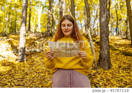 Active young woman holding and reading a map while taking a hiking break, having fun and relaxing while spending autumn day outdoors Active young woman holding and reading a map while taking a hiking break, having fun and relaxing while spending autumn day outdoors 95707119
